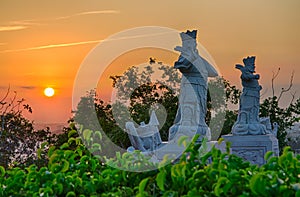 View of the sunset from a Buddhist temple on the mountain. Golden sky. Marble statues of warriors in the middle of the trees