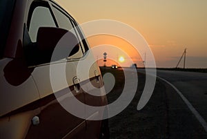 View of the sunset, country road and reflection of sunset on the side surface of a passenger car. The shot was taken in Russia.