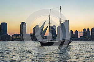 View during sunset on an old sailing ship sailing on the Hudson River and the sun setting between the sky-line of Jersey City, New