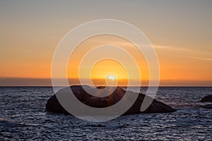 View of sunset over ocean with big rock