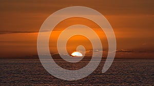 View of sunset with sun going down on the horizon with dramatic orange colored sky viewed from the coast of Taurito, Gran Canaria.