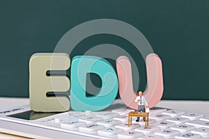 View of teacher figurine standing on a calculator around EDU letters