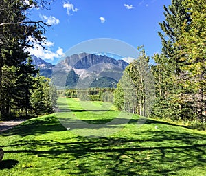 A view from the tee box looking down a tough par 4 lines with trees and the rocky mountains in the background.