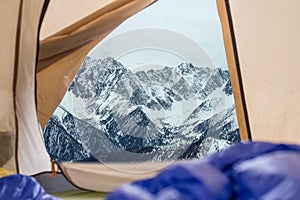 View from tent on snow-capped mountains. Trips and expeditions in the wild. Concept of camping