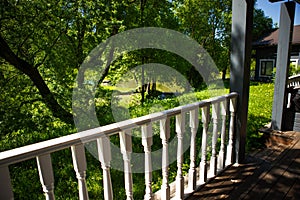 View from the terrace of a country wooden house to the garden through the white wooden railing of the terrace.