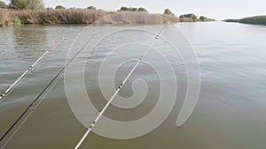 View of three fishing rods over water with nibble hanging from fishing boat.