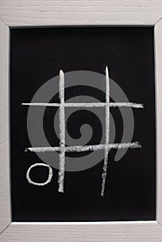 View of tic tac toe game on blackboard with chalk grid and naught on wooden surface photo