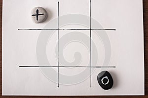 View of tic tac toe game with stones marked with naught and cross on white surface photo