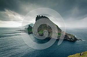 View at the Tindholmur islet with its high steep vertical wall, Mykines island in the background, Faroe Islands