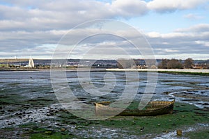 a view of tipner lake in Portsmouth, UK with an old wooden boat in the foreground at low tide also showing Brent Geese on the