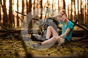 View of tired young woman in forest who is sitting near fallen tree