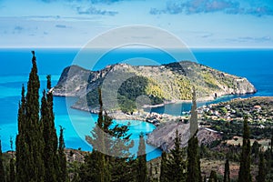 View to Assos village in sun light and beautiful blue sea. Cypress trees in foreground. Kefalonia island, Greece