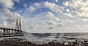 View to Bandra Worli Sea Link bridge through the rocky beach under fluffy clouds, Mumbai, India