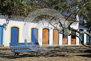 View to colonial house facades with colorful wooden doors in sunshine with a blue bench and tree branches in front, historic town
