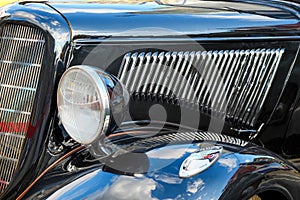 View to front grill, hood,fender and headlight  of a restored  classic vintage black car with blue cloudy sky reflection