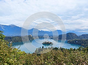 view to the island on lake Bled and dark blue mountains. Slovenia under white clouds