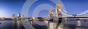 View to the lit skyline of London, UK, during evening: from the Tower Bridge along the river Thames