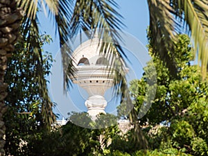 View to the Riyam Park monument dome through the palm leaves. Muscat, Oman.