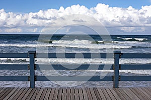 View to the sea waves under blu sky with dense clouds on skyline from pier with blue wooden fence on bright sunny ay