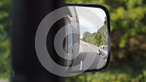 View to side mirror of truck with empty road at background. Lorry driving through countryside on sunny summer day