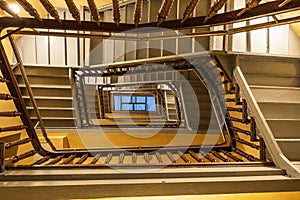 View to top of highlighted high and old square spiral staircase with decorative wooden railings and yellow ceilings