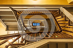 View to top of highlighted high and old square spiral staircase with decorative wooden railings and yellow ceilings