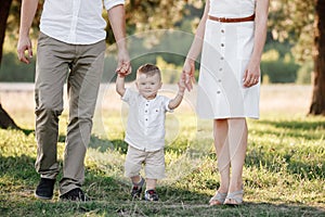 View on toddler. Mother, father hold hands son walk in the park. Young family spending time together on vacation, outdoors. The