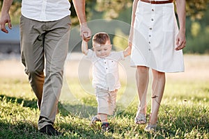 View on toddler. Mother, father hold hands son walk in the park. Young family spending time together on vacation, outdoors. The