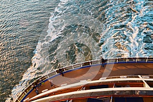 View from the top at the back deck of the cruise ship, leaving foamy trace on the water and waves in the ocean during sunset.