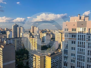 View from the top of the city on residential blocks of high rise buildings across blue sky and white clouds. Building infrastructu