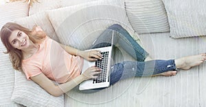 Girl student working with laptop sitting on sofa and looking at camera.