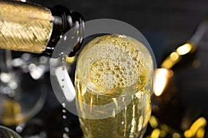 View from top glass of sparkling champagne with bubbles and foam. Close up pouring white wine from bottle into glass