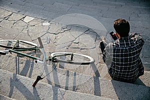 View from top on man with cell phone, sitting on steps near the bike