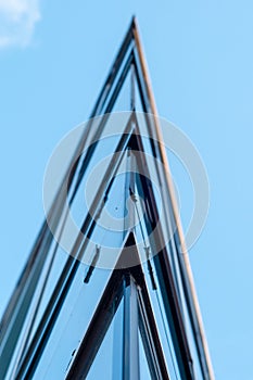 View at top of modern office building with glass and steel under blue sky, reflections and selective focus.