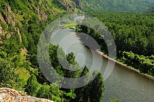 View from the top of the mountain to the bend of a beautiful river flowing through a dense coniferous forest along a rocky ridge