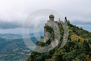 View from the top of the mountain to the medieval fortification. Dramatic mystical weather with fog. Castle in San Marino Seconda photo