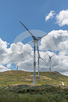 View of a top mountains landscape with a wind turbines, green herb fields and dirty road, cloudy sky as background