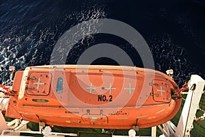 View from top on the orange colour life boat with reflective tape stickers secured with davits and safety hooks.