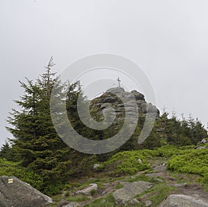 View on the top peak of Jizera mountain rock with big cross in moody day, fog tree background