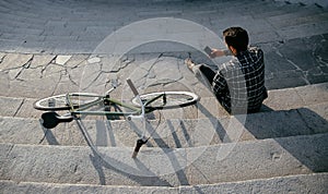 View from top on young man with smartphone, sitting on steps near the bike