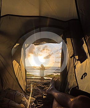 View from the tourist tent to the dawn sea. Guy lies in a tent. The girl on the background of the sunset sea