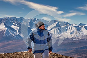 View of a tourist walking in the mountains. White snowy mountain ridge and beautiful blue cloudy sky as a background and slightly