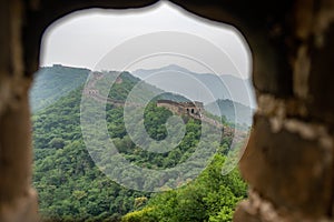 view from the towers window of Great Wall of China with a green trees and rocky mountains in the background.