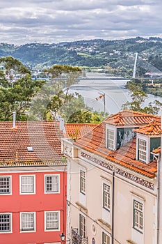 View of traditional classic buildings, with blurred Mondego river and Rainha Santa Isabel Bridge as background in Coimbra, photo