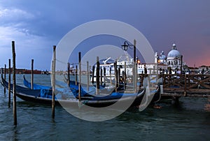 View of traditional Gondolas on Canal Grande with Basilica di Santa Maria della Salute church a cloudy evening . Venice , It