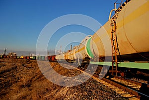 View of the train of cisterns and wagons at sunrise against the blue sky.