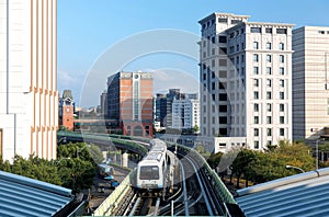 View of a train traveling on elevated tracks of Taipei Metro System between office towers under blue clear sky