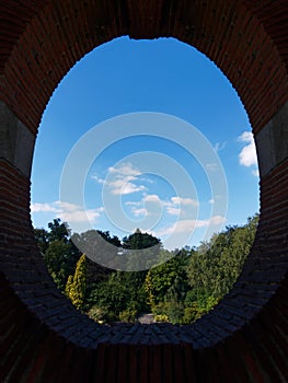 Trees and blue sky with clouds seeing through oval shape stone window