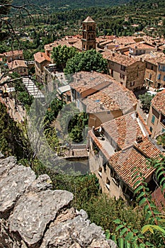 View of trees, house roofs and belfry under sunny blue sky in Moustiers-Sainte-Marie.