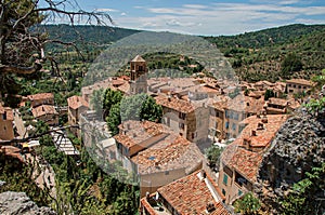 View of trees, house roofs and belfry under sunny blue sky in Moustiers-Sainte-Marie.